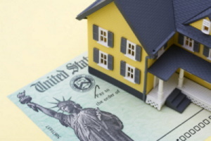 A house replica is placed on an imitation of a dollar bill - Manning Insurance Services.